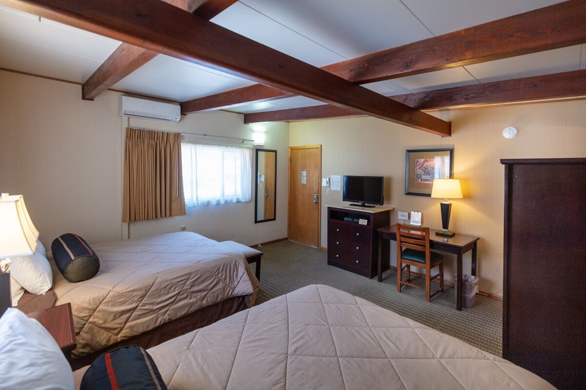 Une chambre d’hôtel avec deux lits, un bureau avec une télévision, une lampe et une armoire.