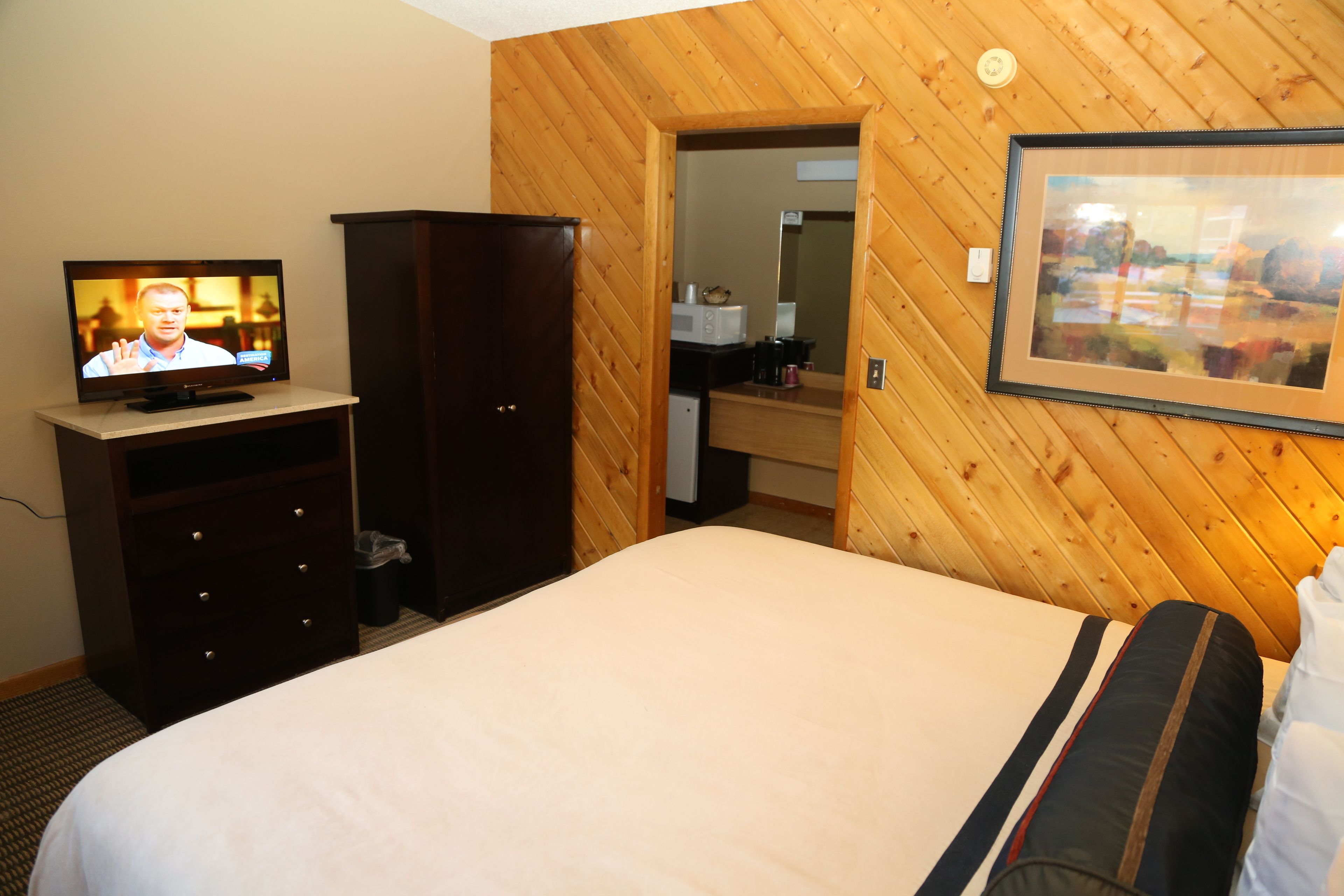 A hotel room with a bed, a television, a wardrobe, a mirror, and a framed picture on the wall.