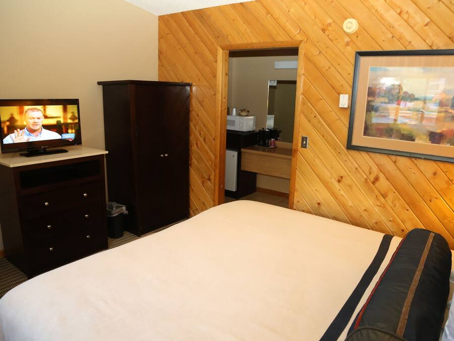 A hotel room with a bed, a television, a wardrobe, a mirror, and a framed picture on the wall.