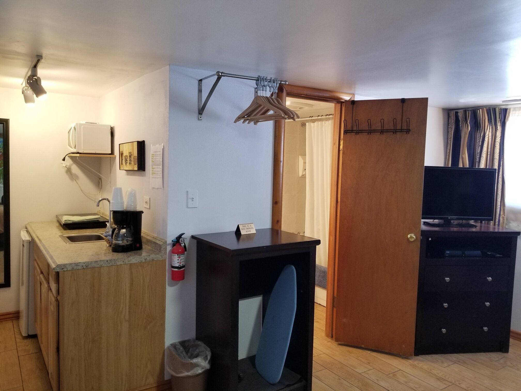 A compact room with a kitchenette, a small seating area, a television, and a wooden door.