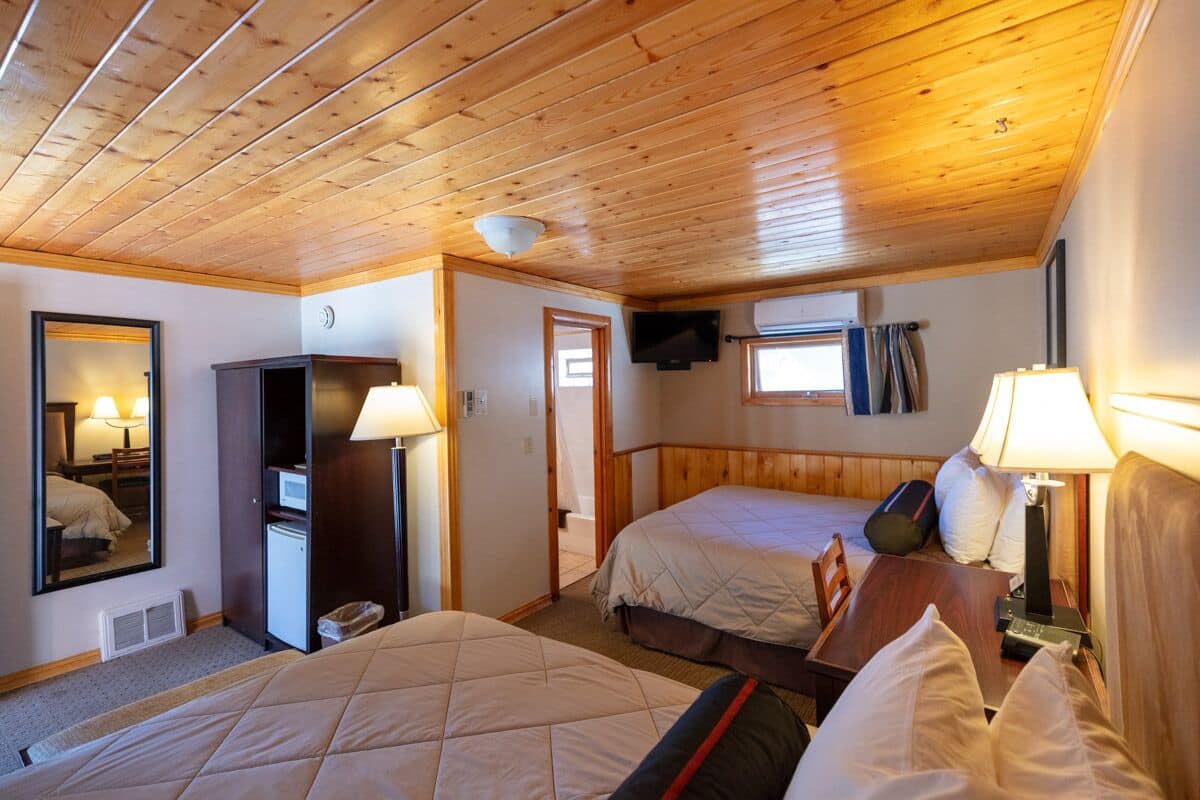 Habitación de hotel con dos camas, techo de madera, televisión, escritorio y espejo.