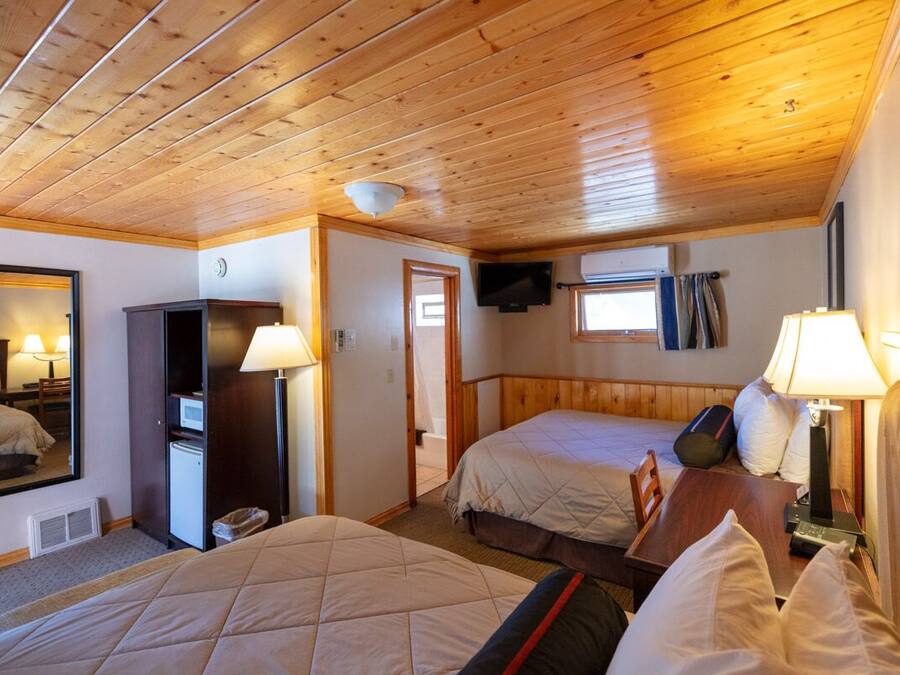 Habitación de hotel con dos camas, techo de madera, televisión, escritorio y espejo.