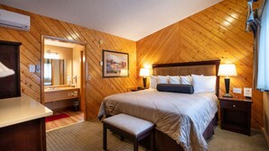 A bedroom with a wooden ceiling, a bed with white bedding, two bedside tables with lamps, a bench, and a mirror.