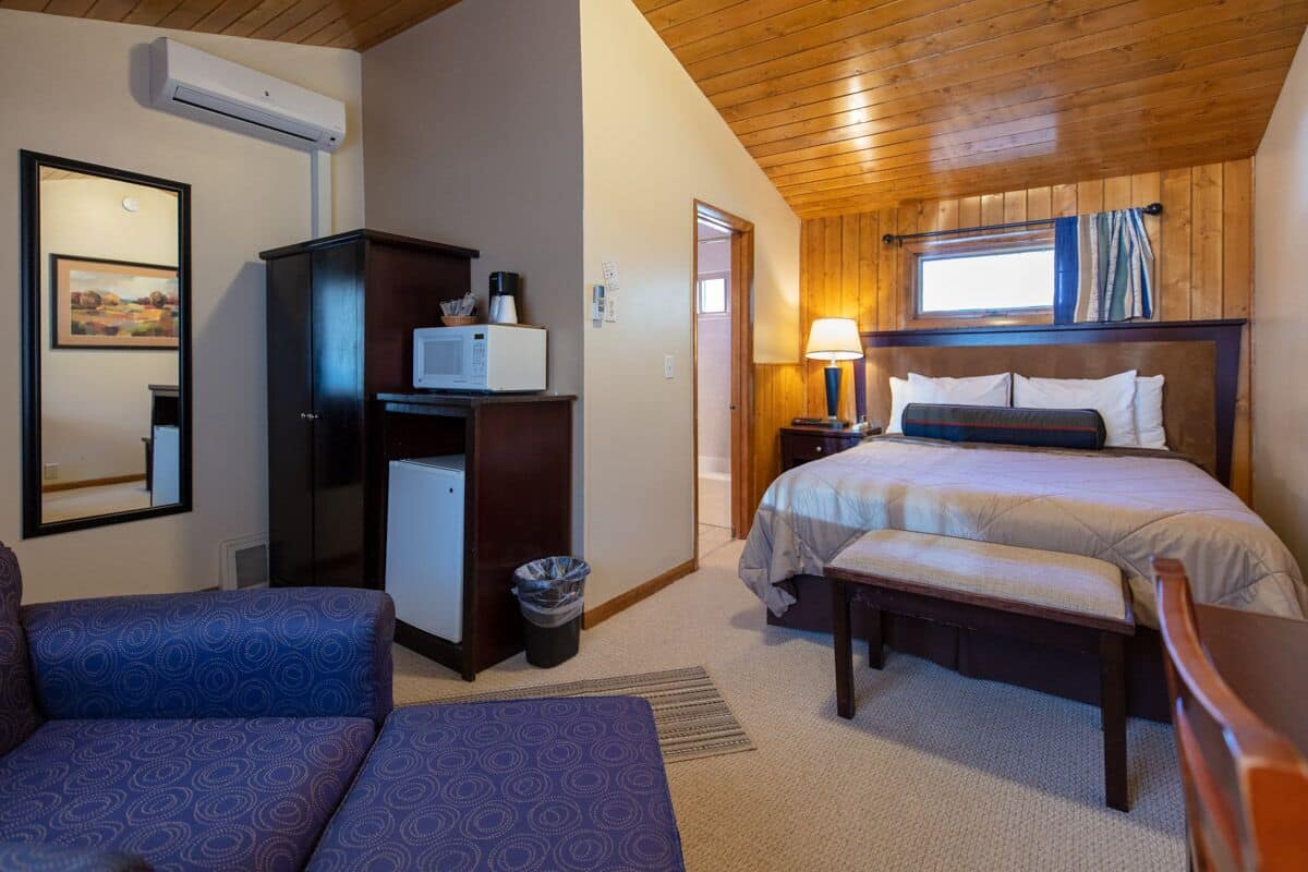 Una habitación de hotel con una cama, un escritorio con computadora, una silla, un sofá y una ventana con cortinas.
