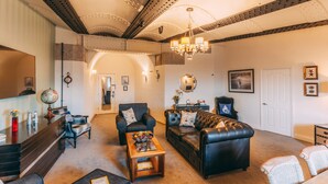 A spacious living room with a leather sofa, armchairs, and a coffee table. A chandelier hangs from the ceiling, and a globe is on a side table. - No Man's Fort (Portsmouth)