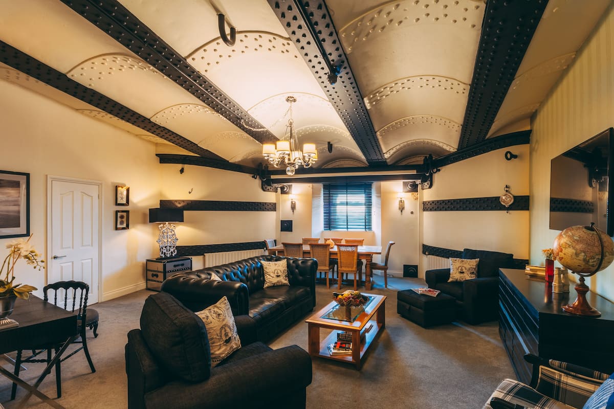 A spacious living room with a high ceiling, leather sofas, a coffee table, and a dining area.