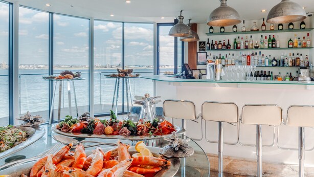 A high-end bar with a panoramic sea view, featuring seafood platters, a well-stocked liquor shelf, and modern bar stools. - No Man's Fort (Portsmouth)