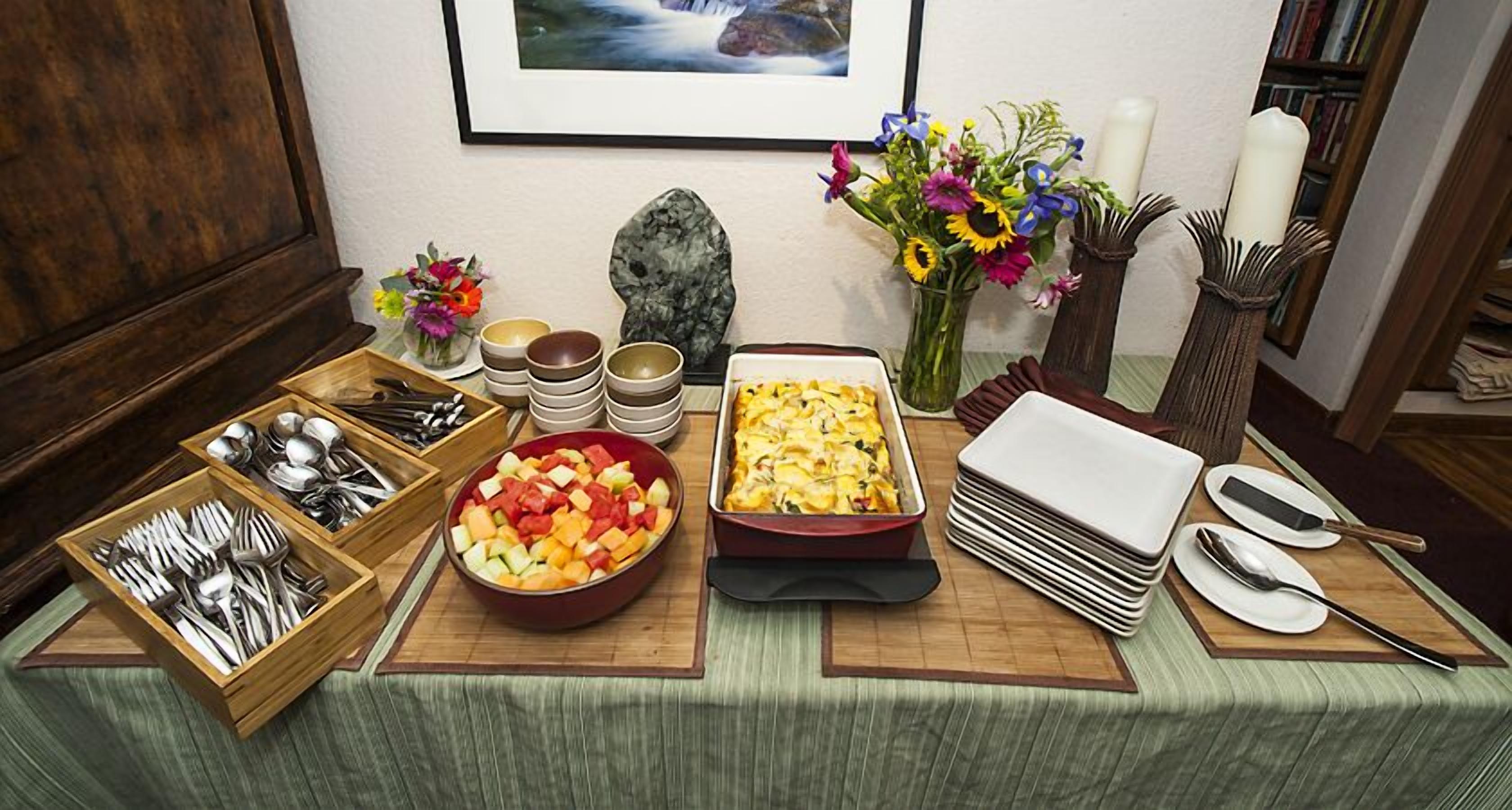 Una mesa de buffet con diversos platos, utensilios y un jarrón de flores.