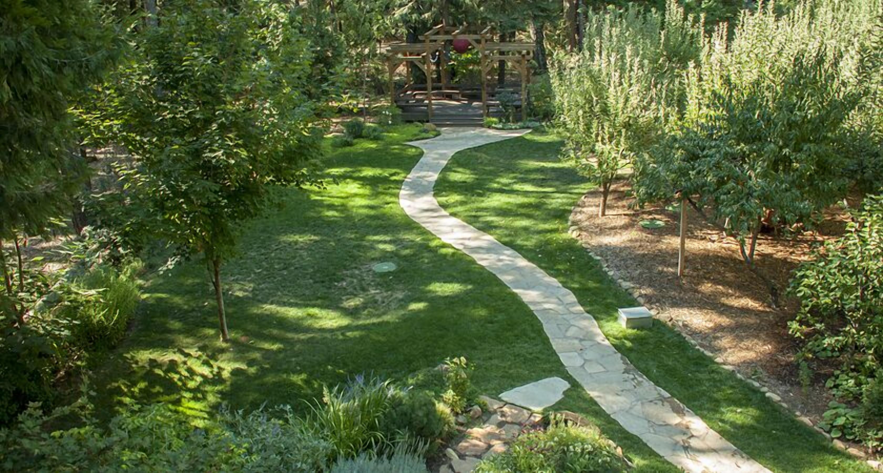 A stone pathway winding through a lush garden with various shrubs and trees.