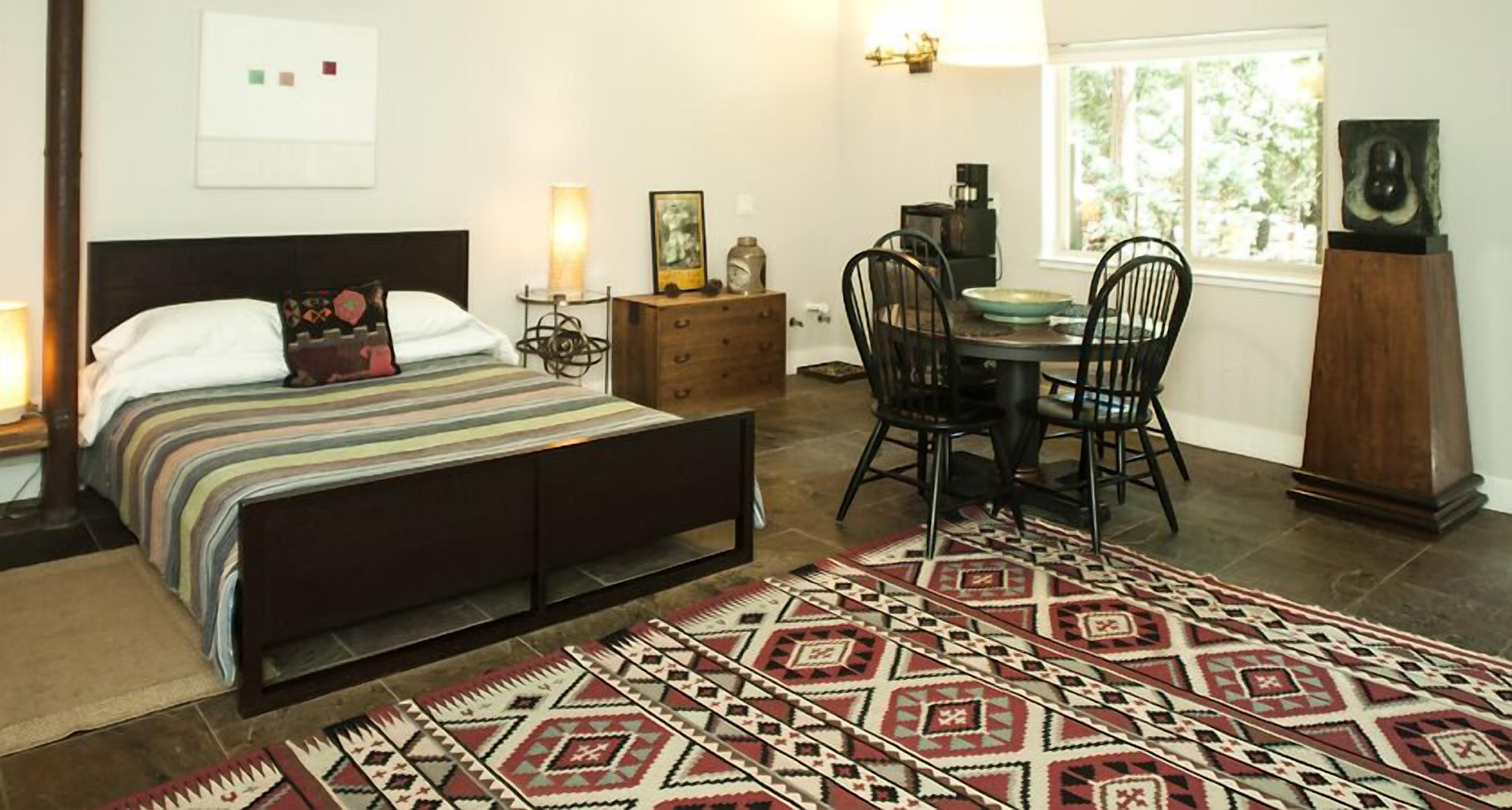Un dormitorio con cama, mesita de noche, lámpara, cómoda, silla, mesa de comedor y alfombra.