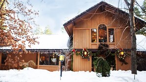 A wooden cabin with a snow-covered roof, surrounded by trees and decorated with Christmas lights and wreaths. - Harmony Ridge Lodge (Nevada City)