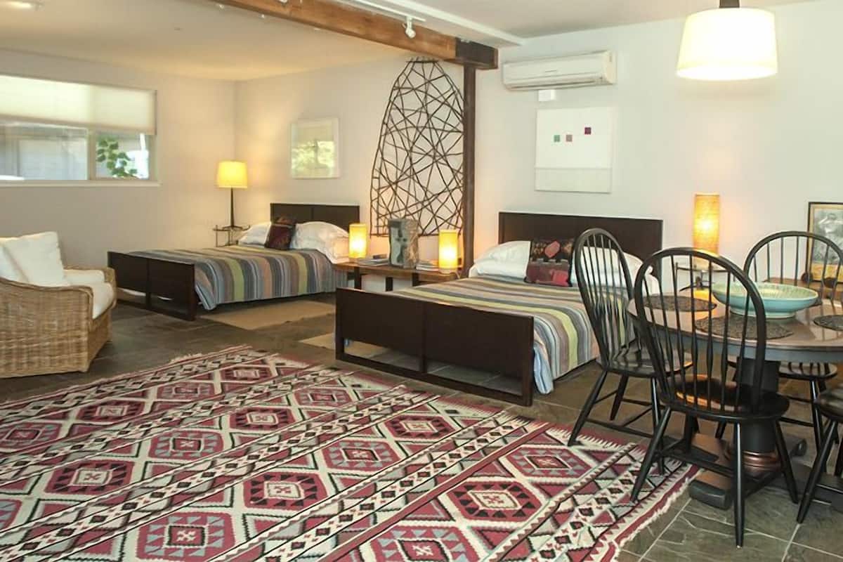 A hotel room with a bed, a dining table with chairs, a patterned rug, and a decorative wall piece.
