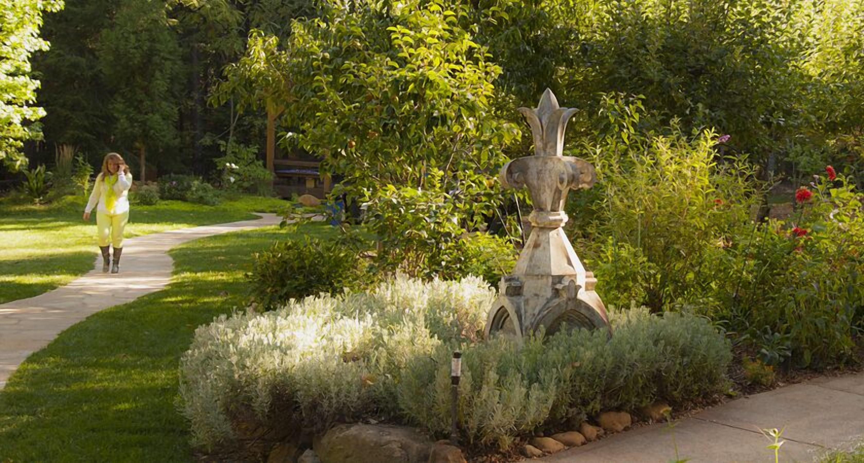 A garden with a stone fountain, a pathway, and lush greenery.