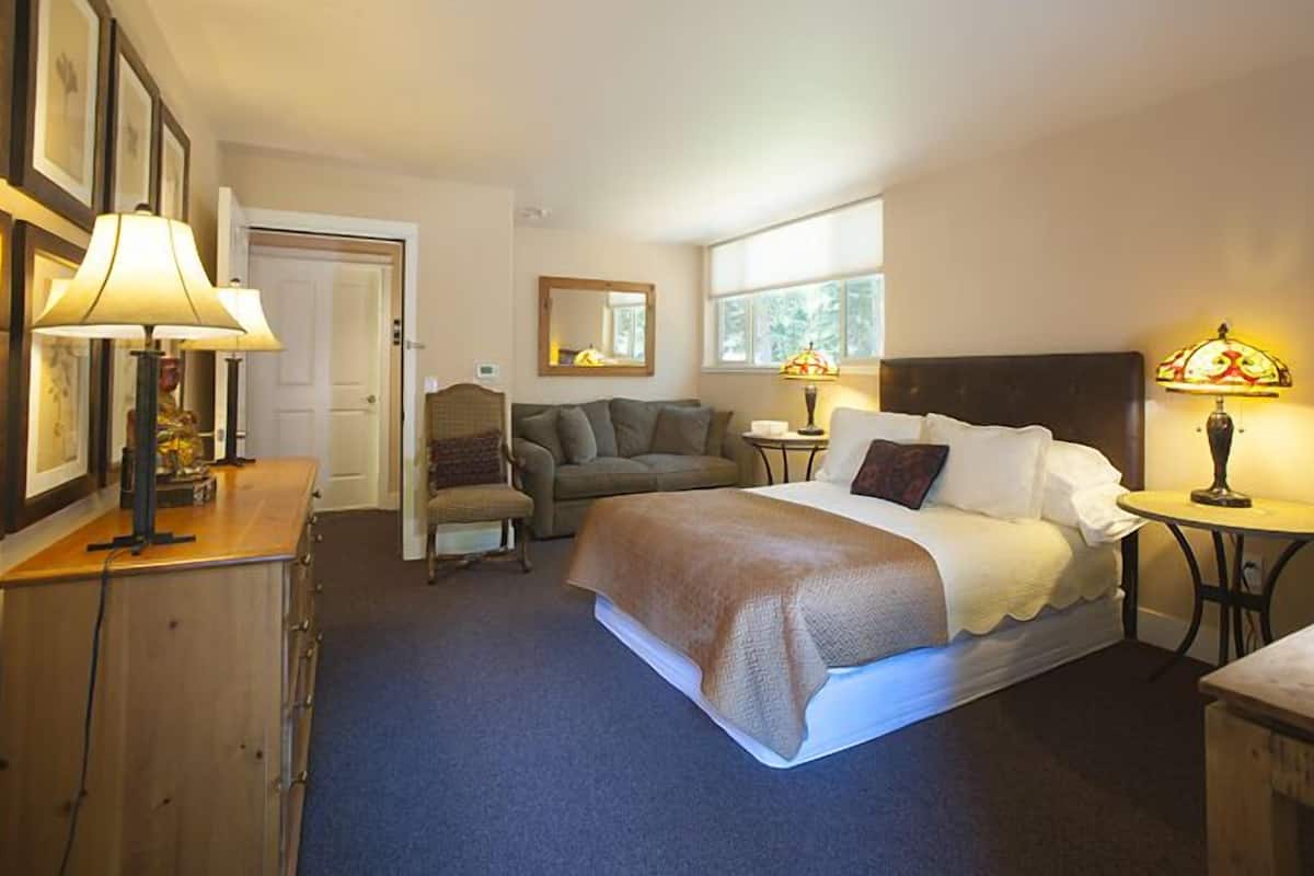 A hotel room with a bed, a sofa, a small table, and a lamp.