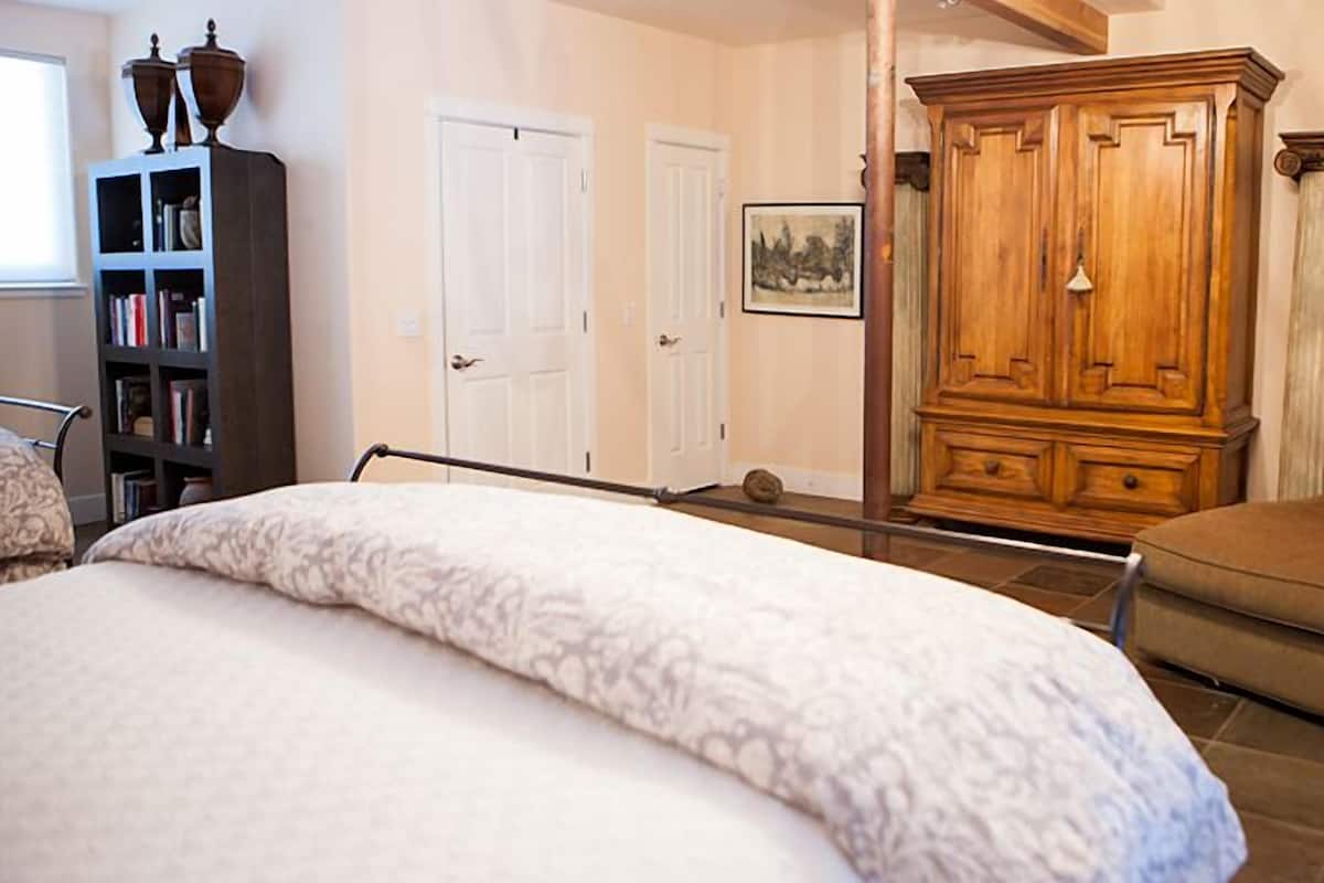 A bedroom with a large bed, a wooden wardrobe, a chair, and a bookshelf.