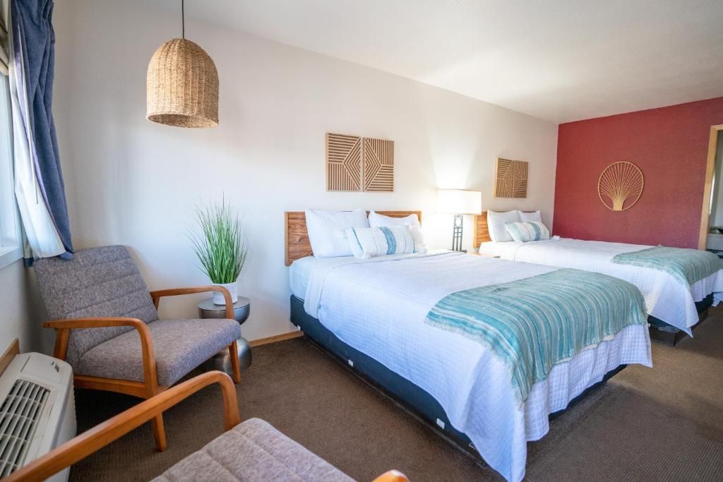 A hotel room with two beds, a chair, a small table, and a hanging light fixture.