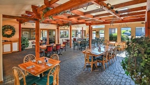 Un restaurant en plein air avec des tables et des chaises en bois, abrité par une pergola en bois et doté d’un sol en briques.