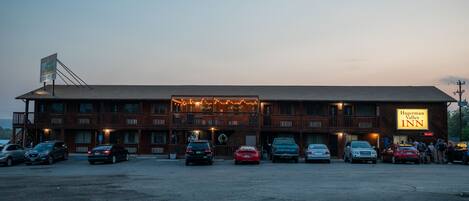 A two-story building with a sign for Hagerman Valley Inn. There are multiple cars parked in front, and a group of people gathered near the entrance.