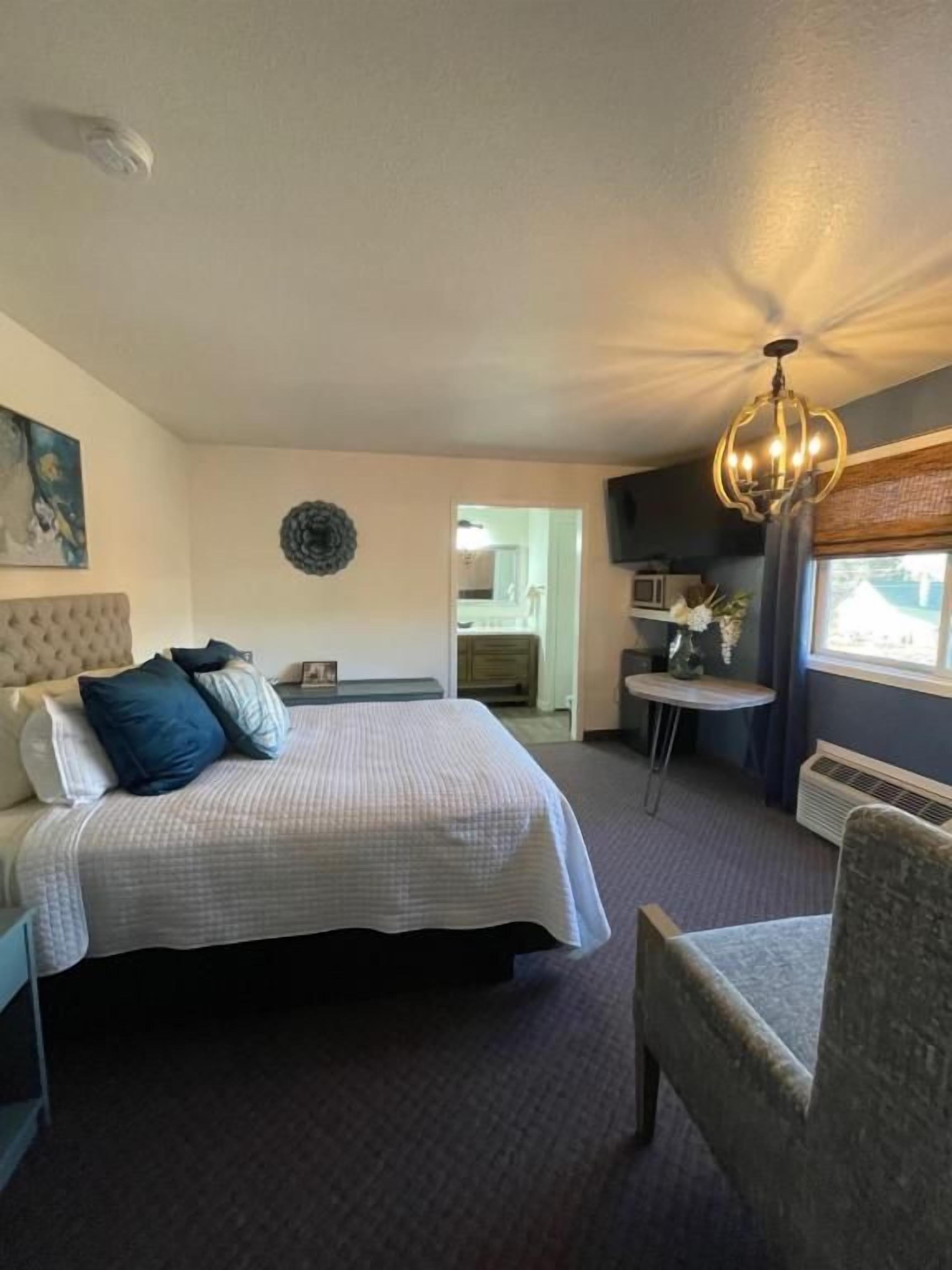 A hotel room with a bed, a chair, a small table, a wall-mounted TV, and a ceiling light fixture.