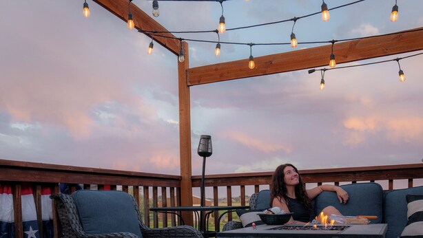 Une terrasse extérieure aménagée avec des meubles en osier, des guirlandes lumineuses et un drapeau.