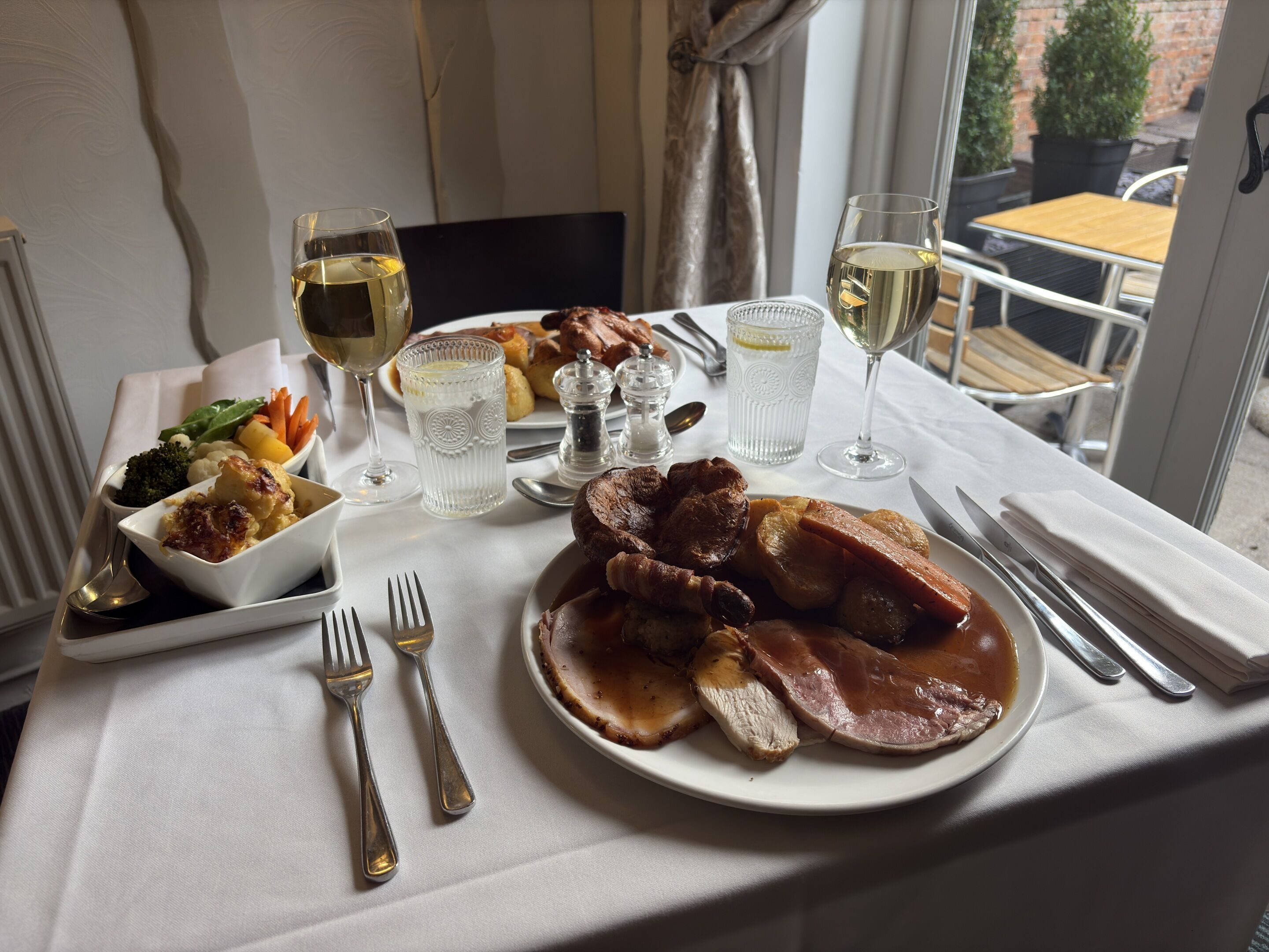 Una mesa de comedor con un plato de comida, copas de vino blanco y cubiertos.