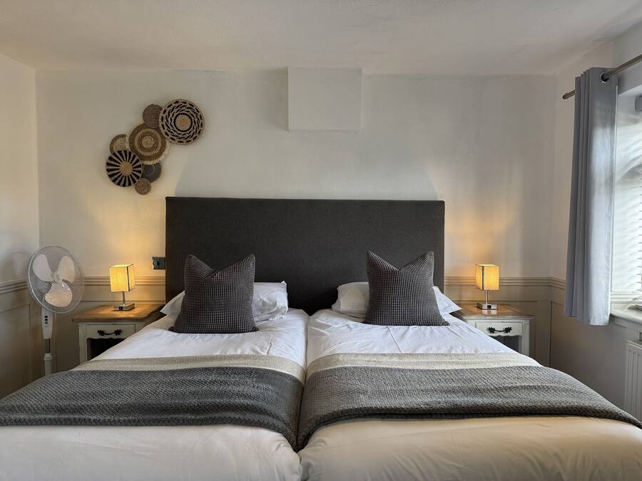 A double bed with a dark headboard, two bedside tables with lamps, a wall-mounted fan, and decorative wall art.