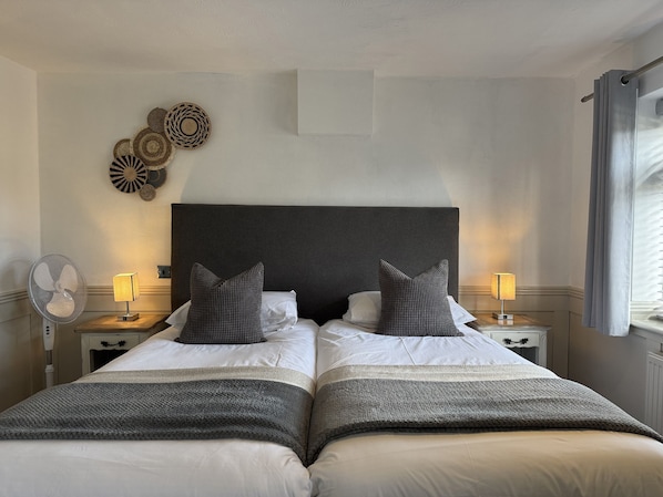 A double bed with a dark headboard, two bedside tables with lamps, a wall-mounted fan, and decorative wall art.