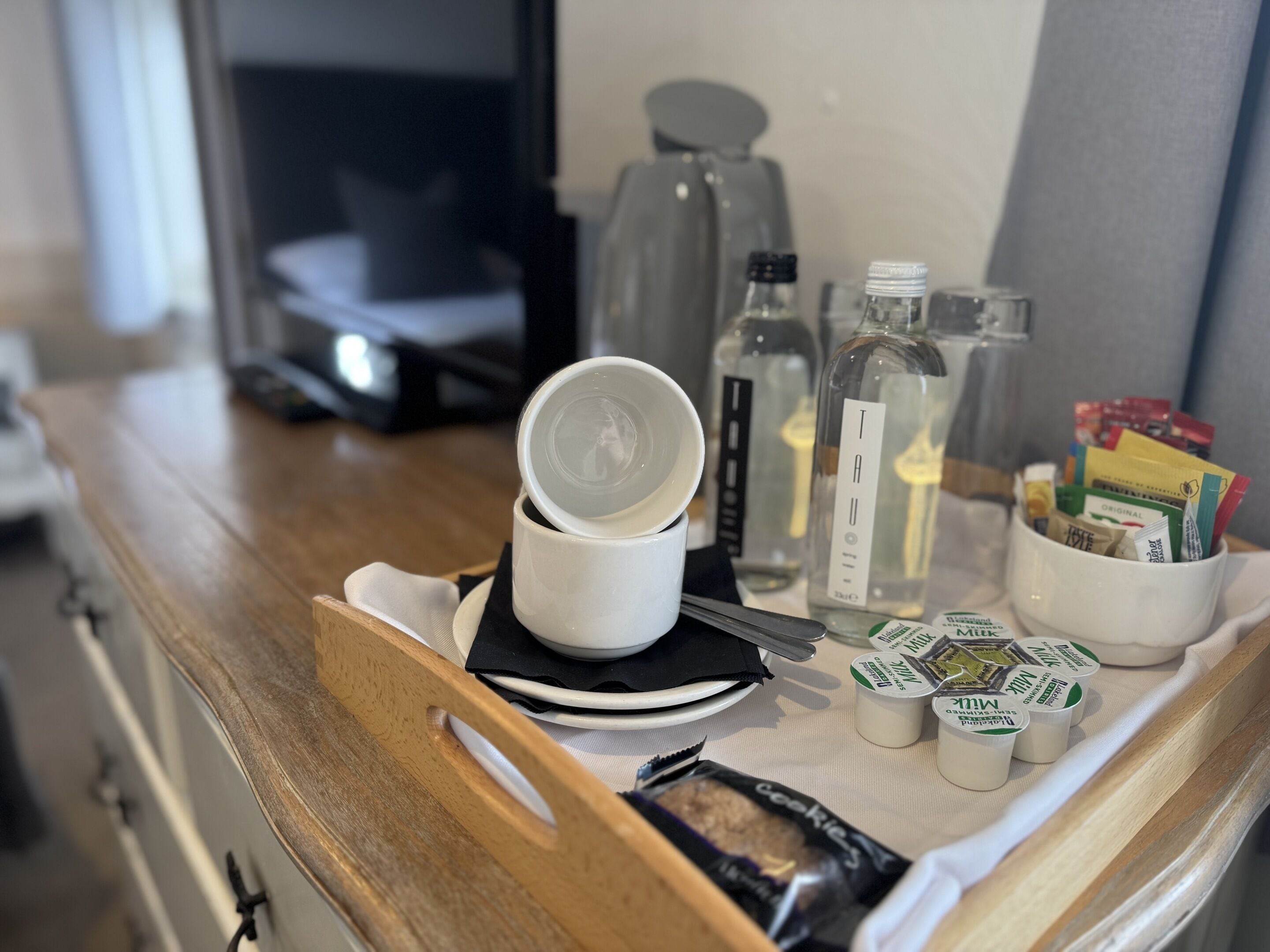 A tray with a white cup, a glass bottle, a glass jar, and a mug filled with tea packets.