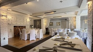 Une salle à manger élégante, avec des tables et des chaises blanches, ainsi qu’une cheminée.