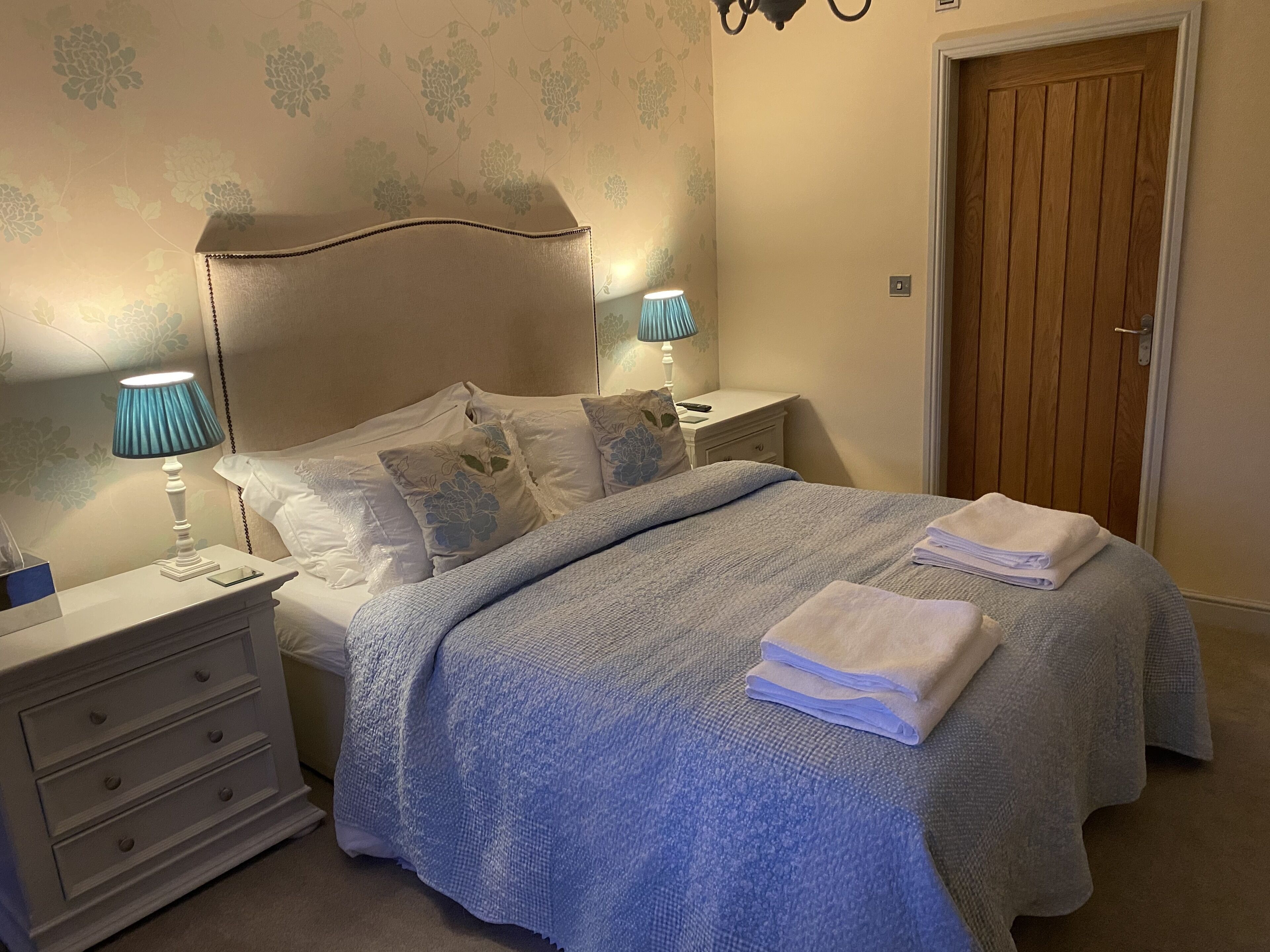 A neatly made bed with a blue blanket, two bedside lamps, and a wooden door in a bedroom.