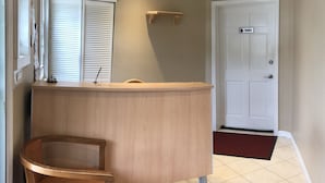 A reception area with a wooden desk, a small chair, a bulletin board, and a private door. - Lantern House Motel (Great Barrington)