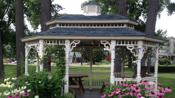 A gazebo with a wooden bench and a picnic table, surrounded by flowering plants. - Lantern House Motel (Great Barrington)