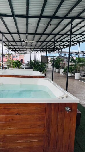 A rooftop pool area with wooden benches and potted plants.