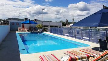 Relax by the pool with lounge chairs and umbrellas, surrounded by a city view.
