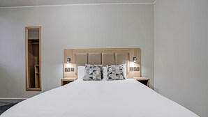 A neatly made bed with a wooden headboard, two bedside tables with lamps, and a built-in shelf unit. - OYO Weaste Hotel (Salford)