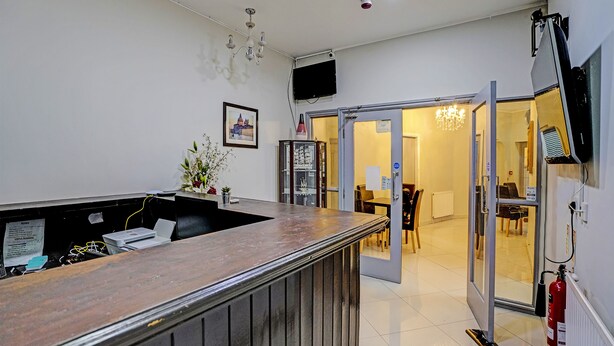 A reception area with a wooden counter, a television mounted on the wall, and a door leading to a dining area. - OYO Weaste Hotel (Salford)