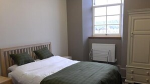 A bedroom with a bed, a nightstand, a radiator, and a cabinet. - The Old School (Islay Island)