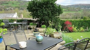 An outdoor patio with metal chairs and a table, surrounded by potted plants and a view of a green landscape. - Cae y Rhedyn Annexe (Crickhowell)