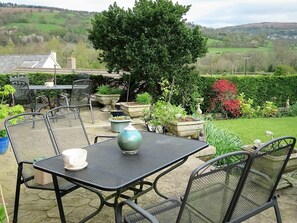 Un patio al aire libre con sillas y una mesa de metal, rodeado de plantas en macetas y vistas a un paisaje verde.