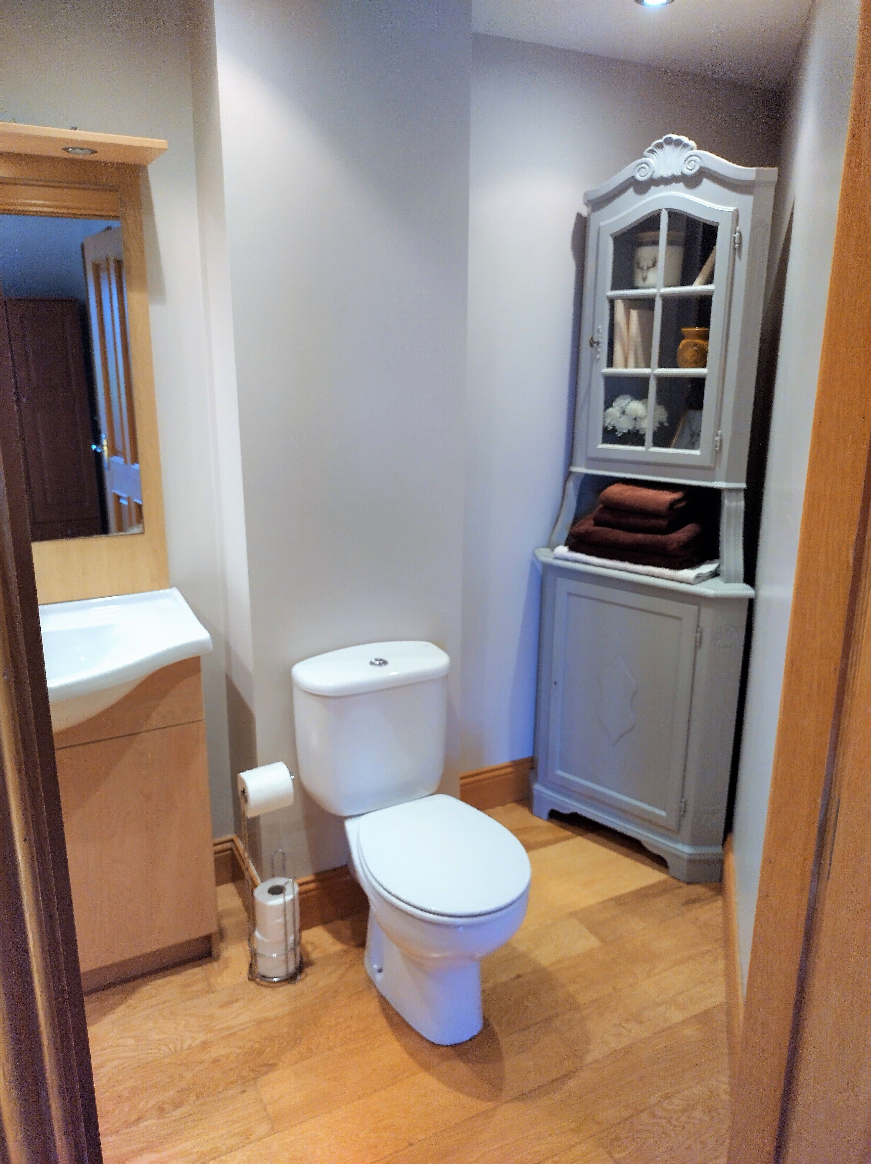 A compact bathroom with a toilet, a small cabinet with a mirror, and a roll of toilet paper on the floor.