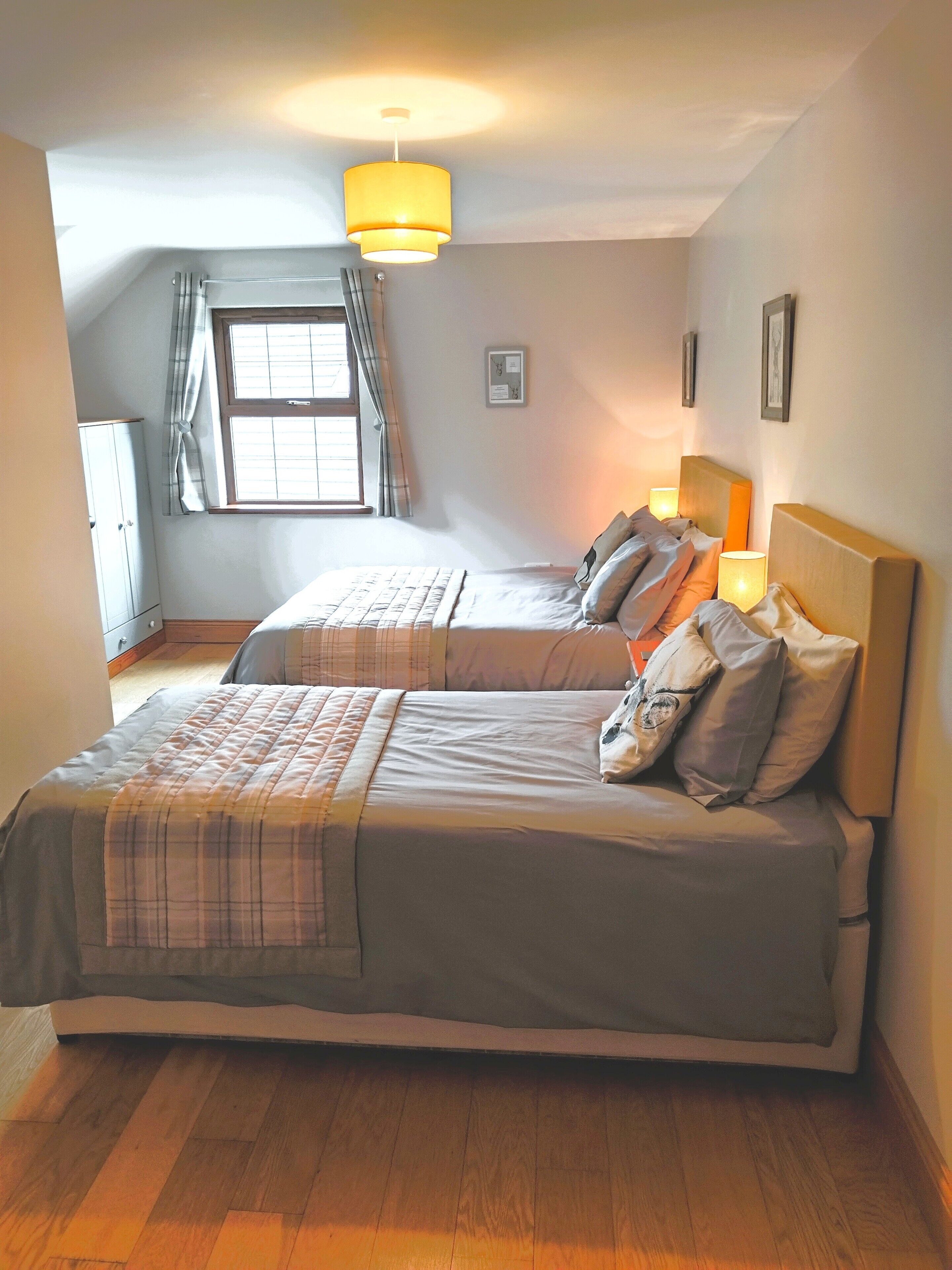 Un dormitorio con dos camas, una ventana con cortinas, piso de madera y una lámpara en el techo.