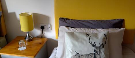 A hotel room with a bed, a nightstand, a lamp, and a wall clock.
