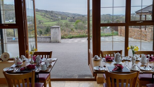 Un comedor con mesas dispuestas para un servicio de té, con vistas a un paisaje pintoresco.