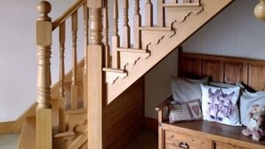 Una escalera de madera con barandilla, un banco de madera con cojines y un techo con estructura de vigas de madera.