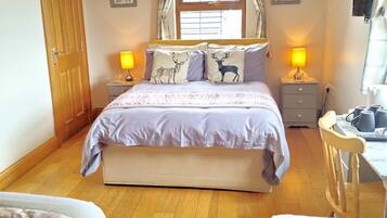 A bedroom with a large bed, two bedside tables with lamps, a wooden desk, and a chair.