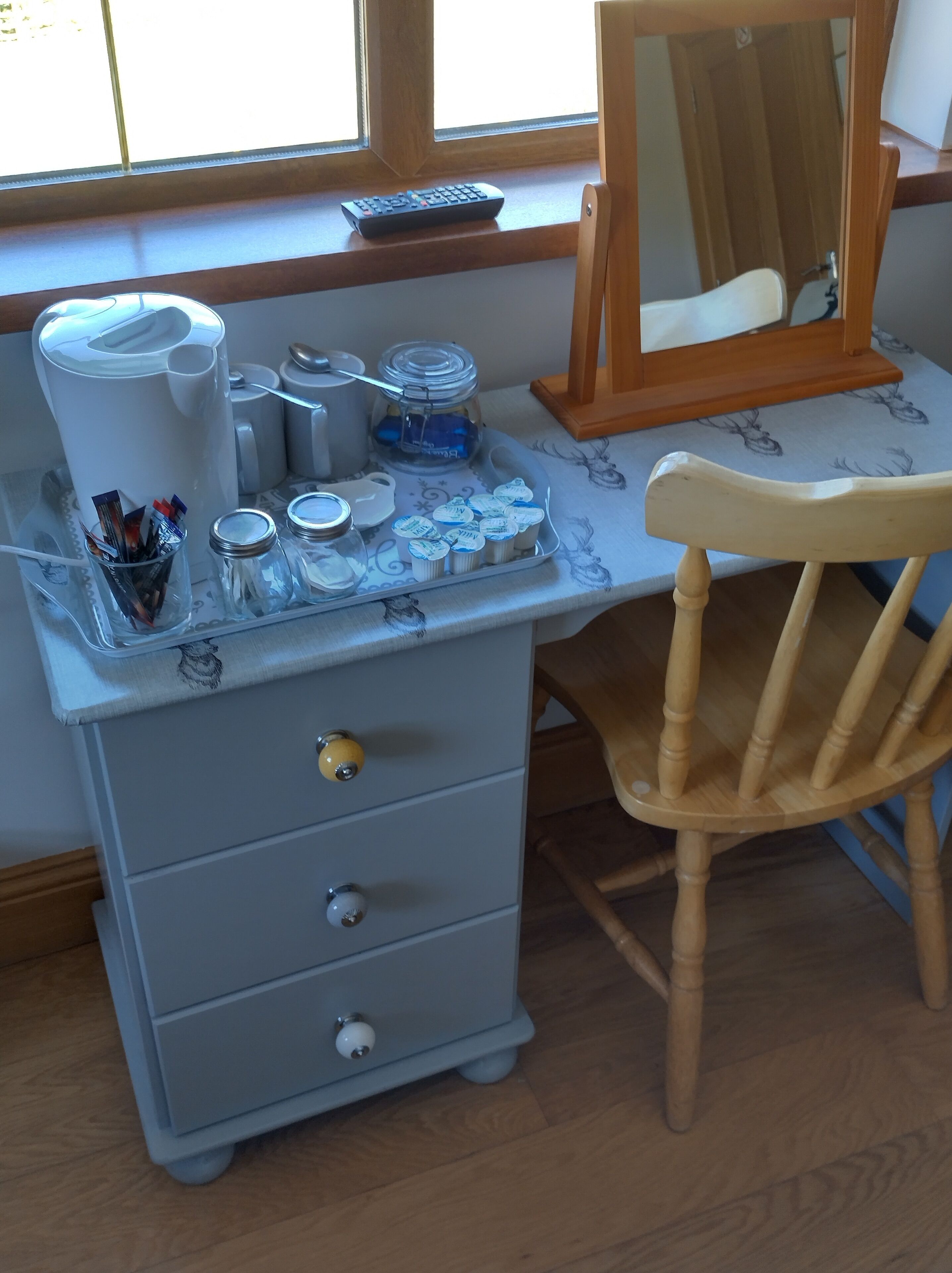 A desk with a mirror, a chair, and a small cabinet with drawers.