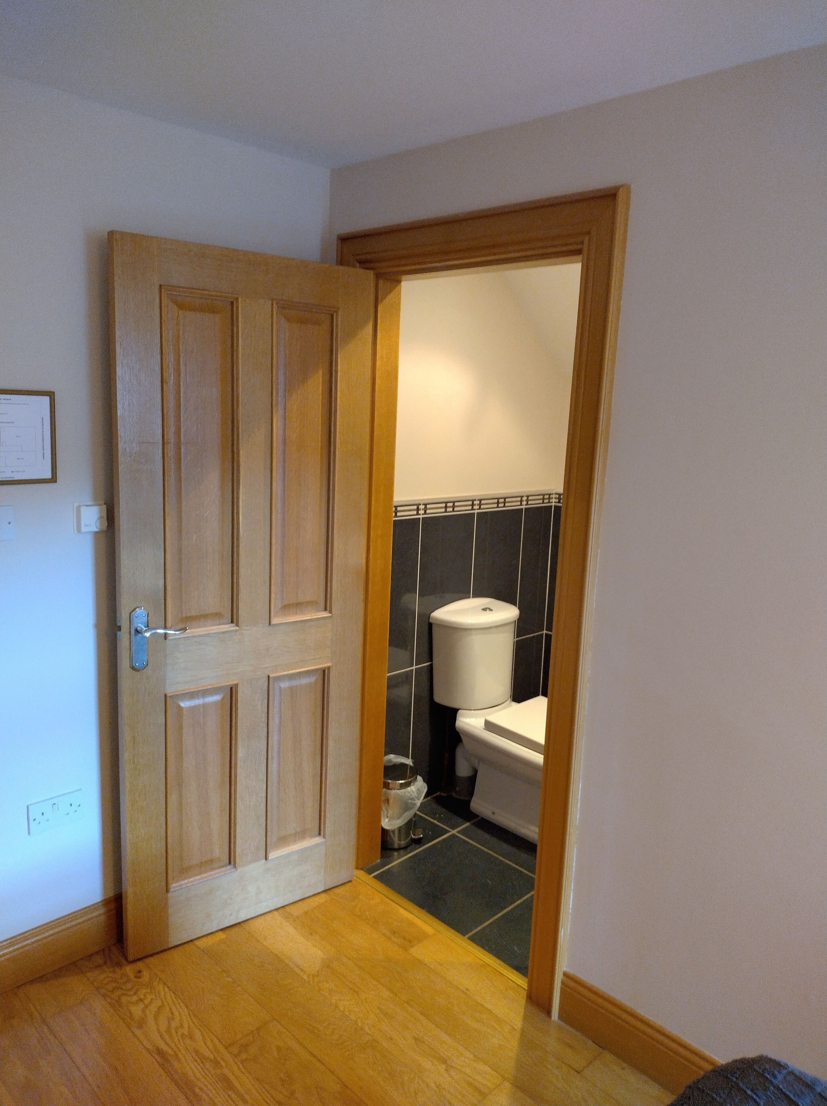 A wooden door leading to a bathroom with a toilet and a trash bin.