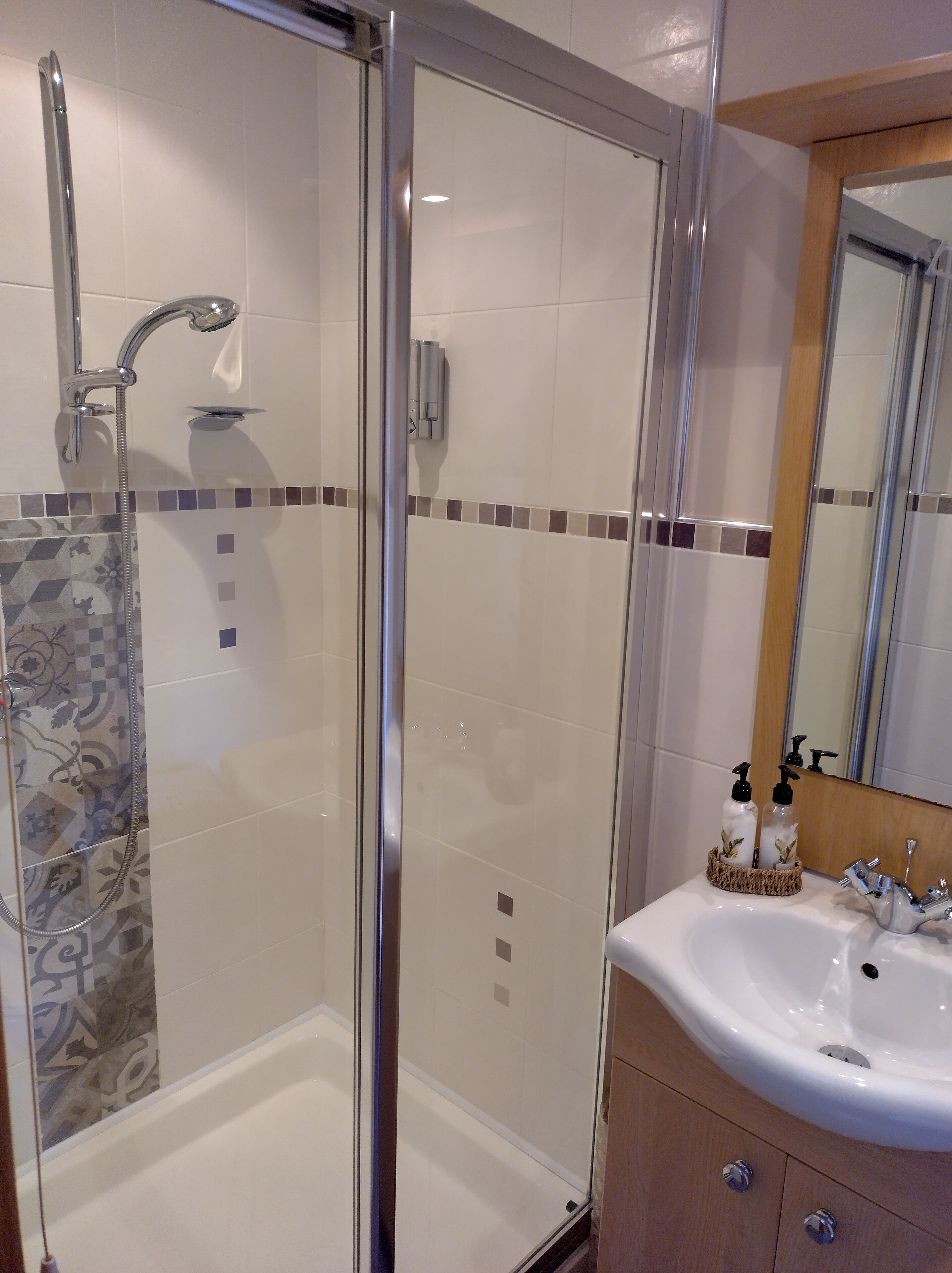 A modern bathroom with a glass-enclosed shower, a white sink with a mirror, and patterned tiles on the floor.