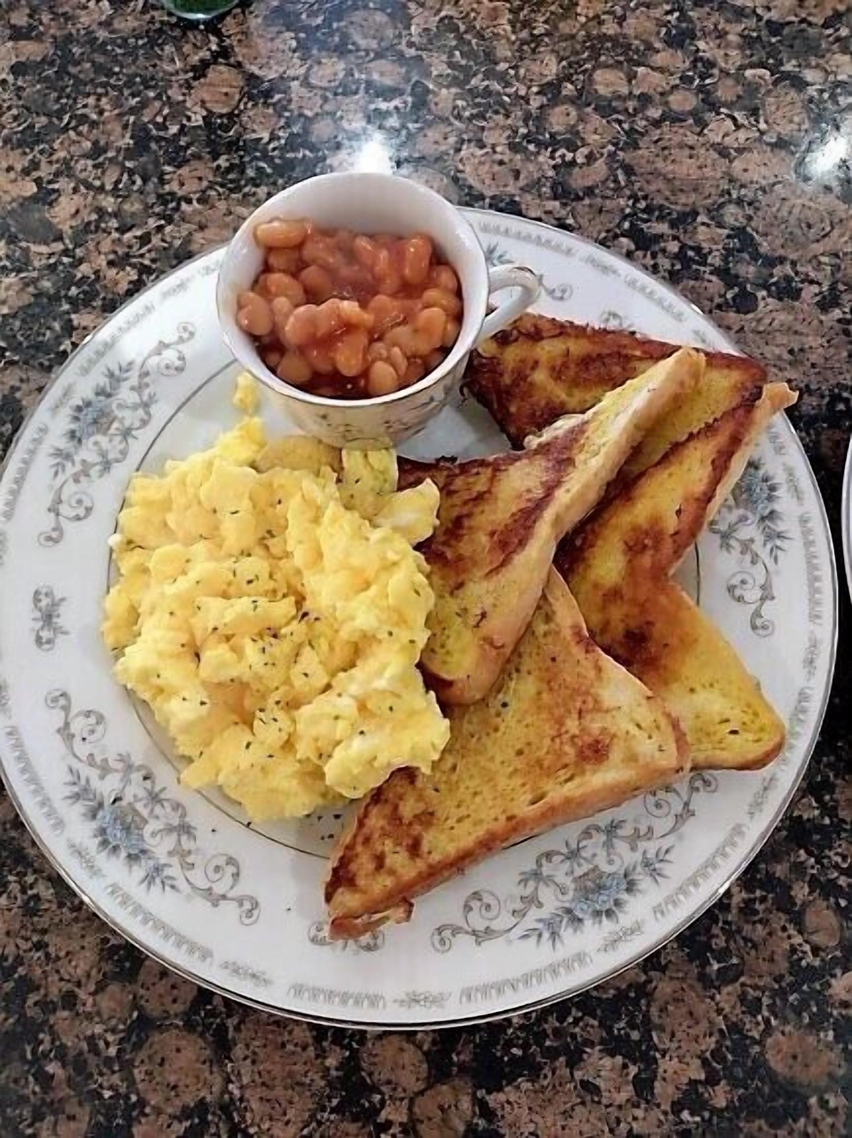 A plate with scrambled eggs, toast, and a small bowl of beans.