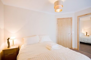 A hotel room with a bed, a nightstand with a lamp, a mirror, and a wooden door. - Bank Guest House (Wick)